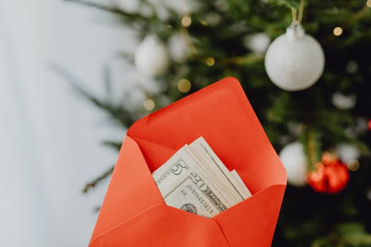 Red envelope with cash set against a decorated Christmas tree symbolizes festive gifting.